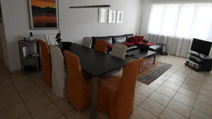 A modern living room with a dining area, a black sofa, a TV, and a large window with curtains. - Casa Leula by Interhome (Ronco sopra Ascona)