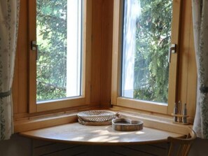 A corner room with a large window, a small wooden table, and two woven baskets. - Chesa Semnadur H8 by Interhome (Sils Maria)