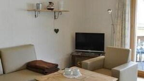 A living room with a sofa, a coffee table, a TV, and a shelf with decorative items. - Chesa Semnadur H8 by Interhome (Sils Maria)