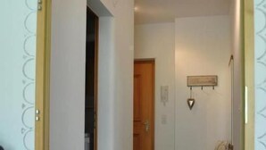 Un couloir avec un sol carrelé, un banc en bois, une décoration en forme de cœur fixée au mur, et une porte au fond.