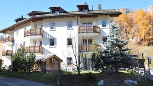 Un edificio de varios pisos con balcones, una cabaña de madera y un cartel que dice 'Muot Marias'.