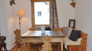 Una habitación acogedora con una mesa y sillas de madera, un sofá con una manta de piel, una lámpara, una decoración de cabeza de venado en la pared, y una ventana con cortinas.