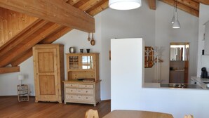 A dining area with a wooden table and chairs, a wooden cabinet, and a kitchen area with a refrigerator and sink. - Chesa Sunasain V11 by Interhome (Sils Maria)