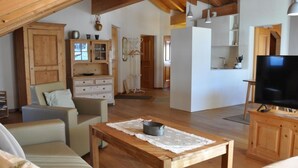A cozy living room with a wooden table, a television, and a sofa. There is a kitchen area in the background with cabinets and a sink. - Chesa Sunasain V11 by Interhome (Sils Maria)