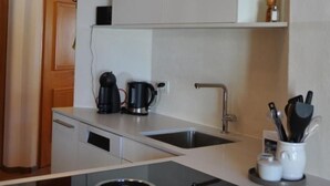 A modern kitchen with white cabinetry, a black induction cooktop, a coffee maker, and a knife block. - Chesa Sunasain V11 by Interhome (Sils Maria)