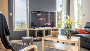 Moderni olohuone, jossa on suuri litteänäyttöinen televisio, jolta näkyy Netflix, sohva, sohvapöytä ja näkymä suurista ikkunoista.