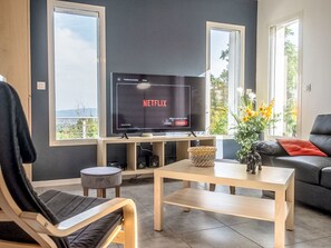 A modern living room with a large flat-screen TV displaying Netflix, a sofa, a coffee table, and a view through large windows. - Ein gemütliches Nest im Herzen der Ardèche Méridionnale by Interhome (Largentière)