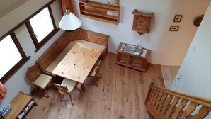 Een houten eettafel met stoelen, een hanglamp, een houten kast en een trap.