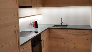 Een kleine keuken met houten kastjes, een zwart aanrecht en een roestvrijstalen spoelbak.