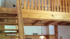 Een loft-achtige kamer met een houten trap, een bank en een hanglamp.