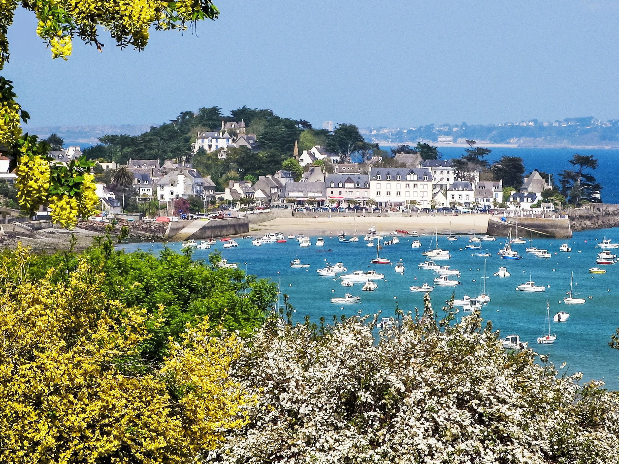 A coastal town with a harbor filled with boats, a sandy beach, and buildings with a traditional architectural style.