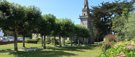 Una iglesia con un campanario alto, rodeada de un jardín bien cuidado con árboles y flores.