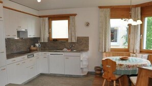 A compact kitchen with white cabinets, a built-in oven, and a window with curtains. - Apartment  by Interhome (Sils Maria)