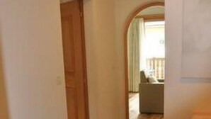 A hallway with a wooden door, a tiled floor, and a view into a room with a chair and a table. - Apartment  by Interhome (Sils Maria)