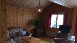 Un salon chaleureux avec un plafond en bois, un canapé, une table basse et un téléviseur posé sur un meuble.