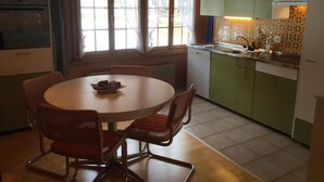 Une cuisine compacte avec un coin repas, comprenant une table ronde et des chaises, une fenêtre avec des rideaux et des meubles de couleur verte.