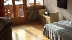 Une pièce confortable avec un plancher en bois, un lit, une chaise, un radiateur et une fenêtre avec des rideaux.