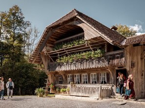 A rustic wooden house with a sloped roof, large windows, and a balcony with plants. - Bärengaden 4-Bettwohnung by Interhome (Hasliberg)