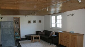 Ein Wohnzimmer mit einem dunkelgrauen Sofa, einem Holzschrank, einem kleinen Tisch, einem Bücherregal und einem Fenster mit Vorhängen.