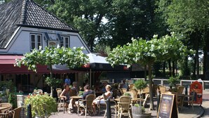 An outdoor seating area with wicker chairs and tables, a building with a tiled roof, and a signboard with text.