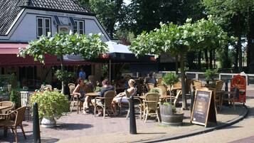 An outdoor seating area with wicker chairs and tables, a building with a tiled roof, and a signboard with text.