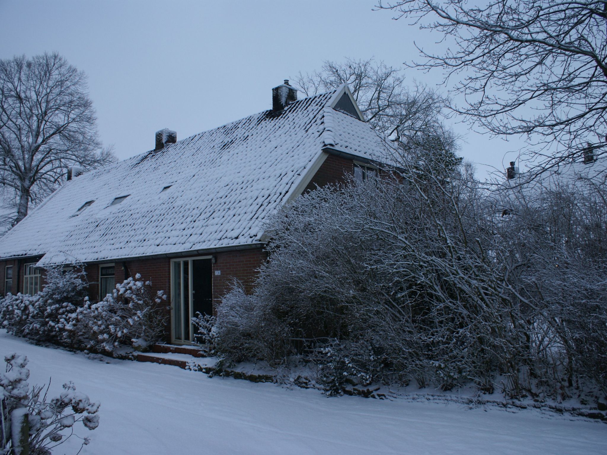 A snow-covered house with a brick exterior and a sloped roof.