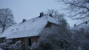 A snow-covered house with a brick exterior and a sloped roof.