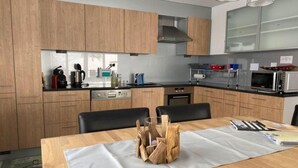 Eine moderne Küche mit Holzschränken, einer Edelstahl-Dunstabzugshaube und einem Essbereich mit Holztisch und -stühlen.