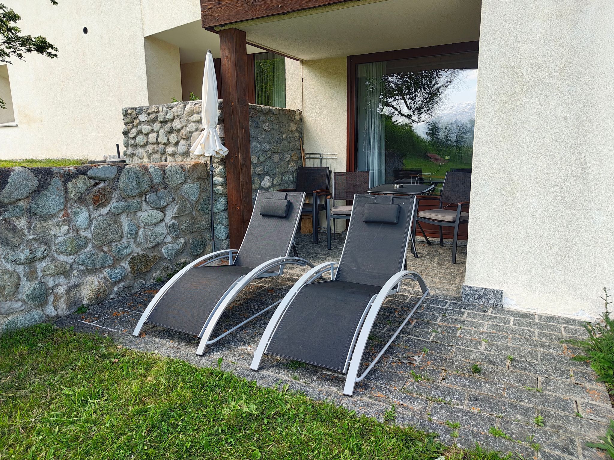 Une terrasse avec trois chaises longues, un mur en pierre et une table avec des chaises.