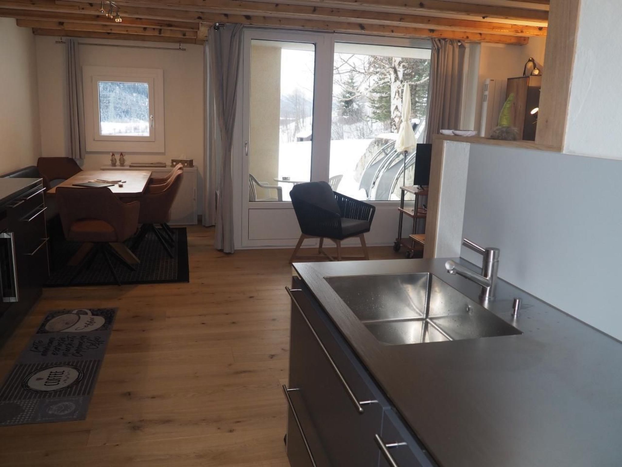 A modern kitchen with a large sink, wooden cabinets, and a dining area with a table and chairs.