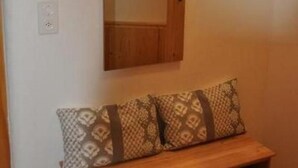 Een houten bank met gekleurde kussens, een spiegel erboven en een klein plankje met een decoratief object.