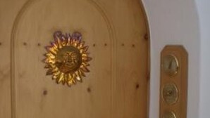 A wooden door with a decorative brass handle and a sun emblem.