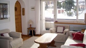 A cozy living room with a wooden coffee table, two sofas, and a view of a snowy street through large windows.