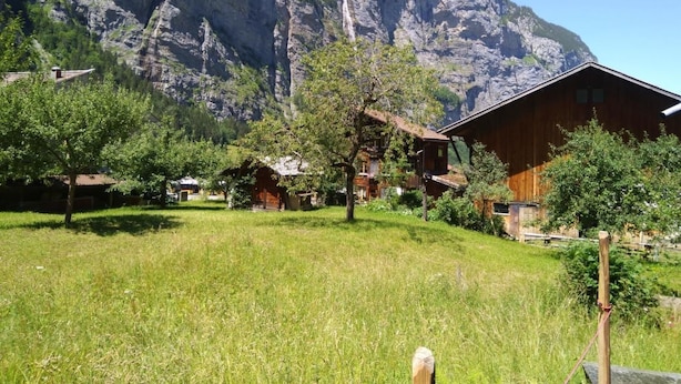 Un village de montagne avec des maisons en bois, un champ verdoyant et une grande montagne en arrière-plan.