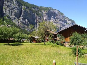 A mountain village with wooden houses, a grassy field, and a large mountain in the background.