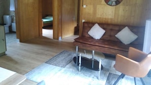 Un salon au parquet en bois, avec un canapé en cuir marron, un fauteuil blanc et une grande horloge murale.
