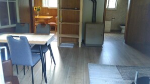 Une pièce comprenant une table à manger en bois, des chaises, une bibliothèque, un radiateur et une salle de bain visible à travers une porte ouverte.