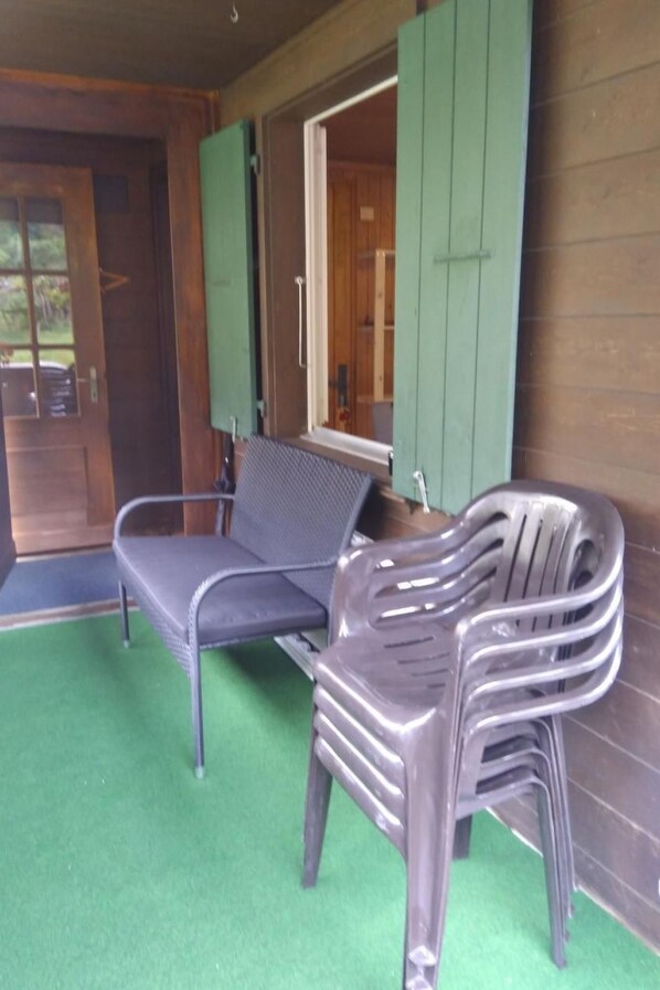 Un espacio de estar techado al aire libre con un banco y una silla, una puerta de madera y un toldo verde.