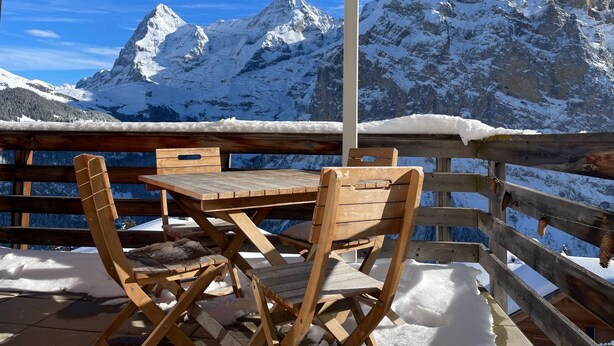 En träveranda med ett bord och stolar, med utsikt över snötäckta berg.