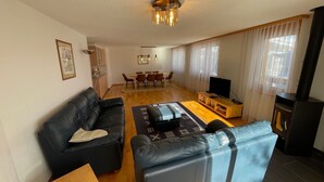 Ett modernt vardagsrum med en svart lädersoffa, ett träbord och en tv. I bakgrunden finns en matplats med ett bord och stolar.