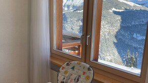 Ett rum med ett träbord, en barnstol och ett fönster med utsikt över bergen.