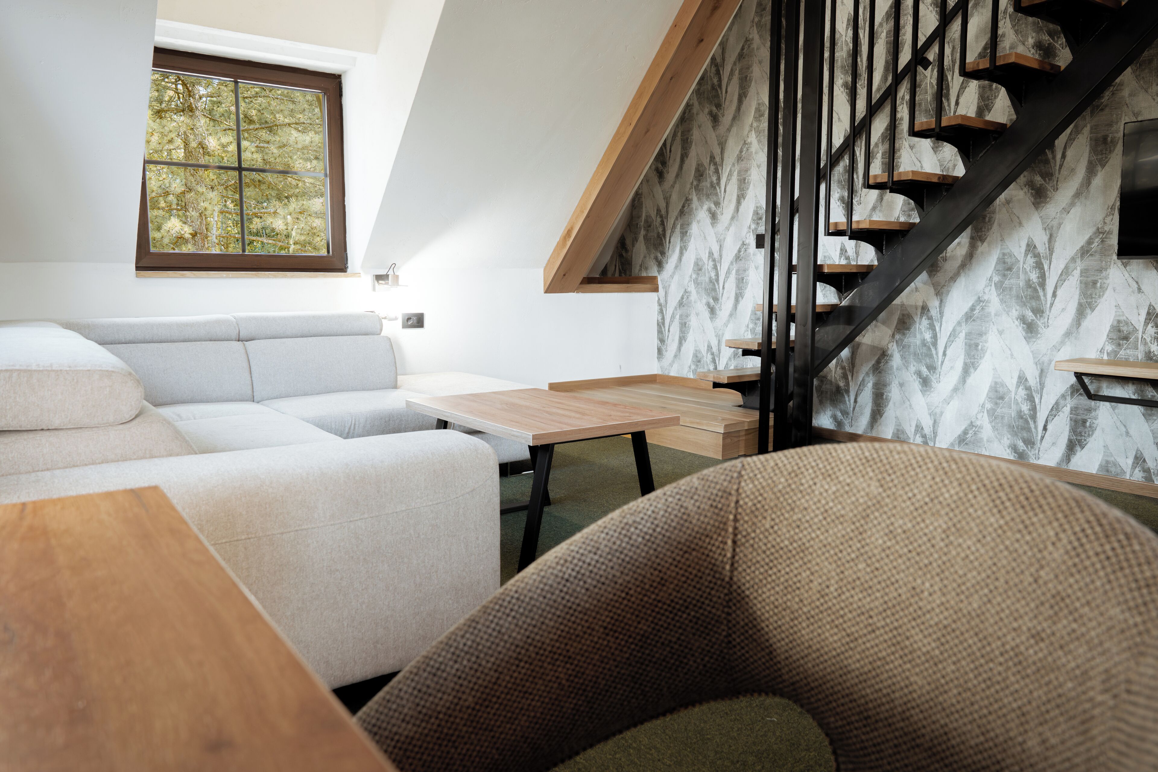 A modern living room with a sofa, a wooden table, and a staircase with a patterned wall.