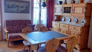 Et hyggeligt værelse med et træbord og stole, en sofa, et skab med dekorative tallerkener og en hængende lampe.
