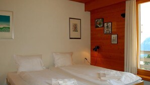 A double bed with white linens, a wooden headboard, and a window with a view of mountains. - Chalet Crystal by Interhome (Lauterbrunnen)