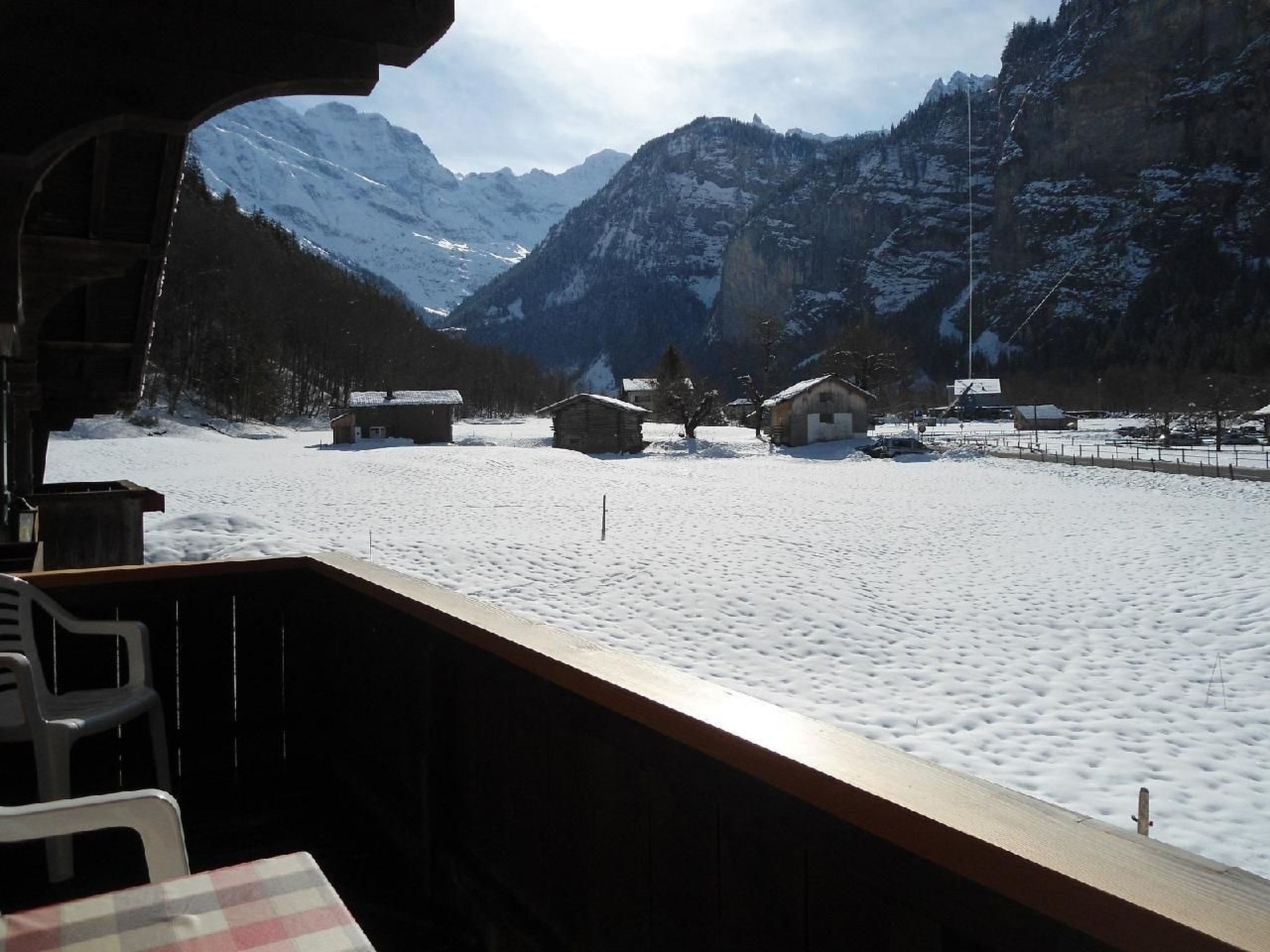 Un paisaje nevado de montañas con una terraza de madera y una mesa.