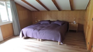 Een slaapkamer met een groot bed, houten wanden, een houten vloer en een raam met gordijnen.