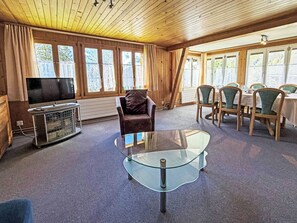 Ein Zimmer mit Glastisch, Fernseher und einer Essecke mit Stühlen und Tisch.