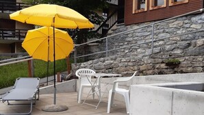 Zona esterna con due ombrelloni gialli, una poltrona grigia e sedie in plastica bianca.