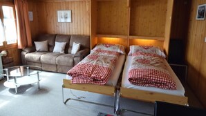 Una stanza accogliente con soffitto in legno, un divano, due letti singoli con copriletto a quadretti, un tavolino e una finestra con tende.
