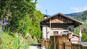 Een rustieke houten chalet met een schuin dak, omringd door weelderige begroeiing en een bergachtig landschap.